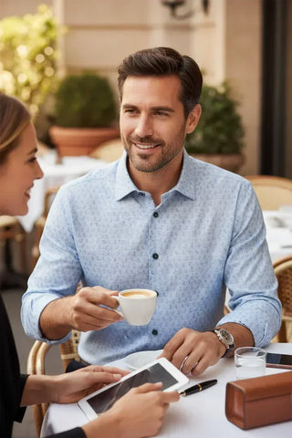 Man in light blue patterned dress shirt enjoying coffee at an outdoor café table
