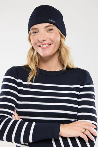 Woman in navy blue knit beanie and navy striped sweater, smiling against white background