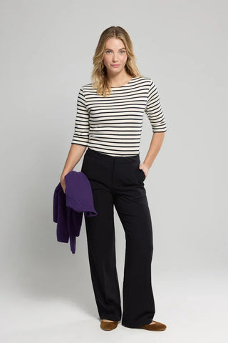 Woman in striped shirt and black wide-leg pants holding purple sweater