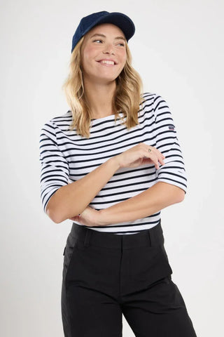 Woman in navy and white striped boatneck shirt, black pants, and navy cap, smiling
