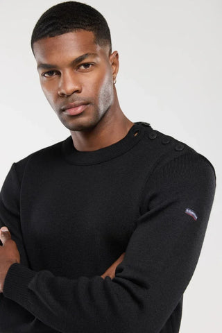 Man wearing black knit sweater with shoulder buttons and small logo patch on sleeve