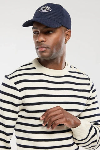 Man wearing a navy Armor Lux cap and cream striped sweater, modern casual fashion
