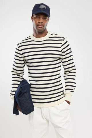 Man wearing navy and white striped sweater, navy cap, white pants, holding denim jacket