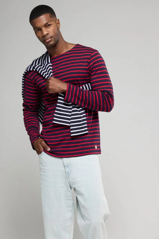 Man wearing a red and navy striped sailor shirt with light jeans, holding another striped shirt
