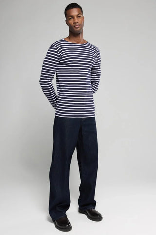 Man wearing navy and white striped long sleeve shirt and dark blue pants, standing against gray background
