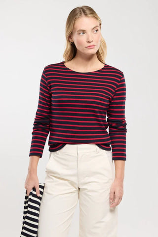 Woman in navy and red striped long-sleeve top with white pants, holding striped garment