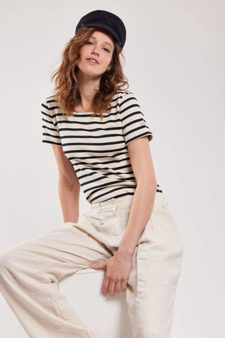 Woman in short-sleeve striped Breton shirt, cream pants, and navy captain hat