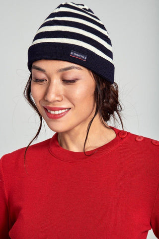 Woman wearing a navy and white striped knit beanie and red sweater with shoulder buttons