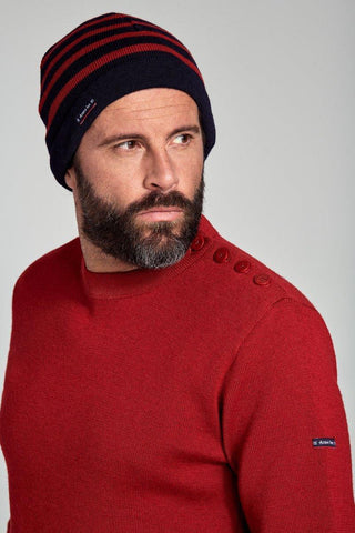 Man wearing a navy and red striped knit beanie and red sweater with button detail