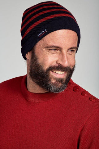 Man wearing a navy and red striped wool beanie and red sweater with shoulder buttons