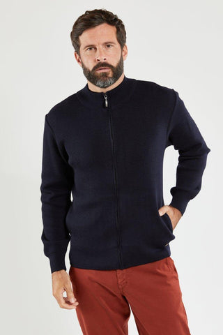 Man wearing navy wool zip-up cardigan and red pants standing against white background