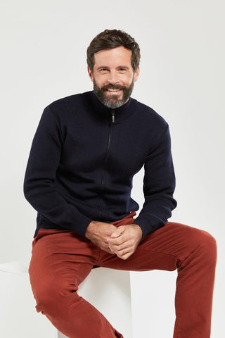 Man wearing a navy wool zip cardigan and red pants, sitting and smiling