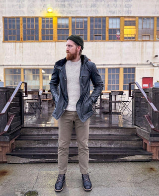 Man wearing a green beanie, black jacket, knit sweater, khaki pants and boots outdoors