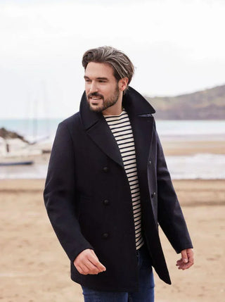 Man in navy wool peacoat and striped shirt walking on beach, casual winter fashion