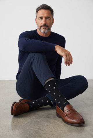 Homme portant des bas Bugatchi noirs à motif fleurs en coton et cachemire, avec pantalon marine et mocassins en cuir.