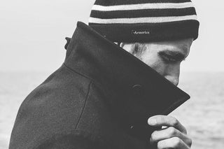 Man in striped knit beanie and high-collar coat by the sea, monochrome style