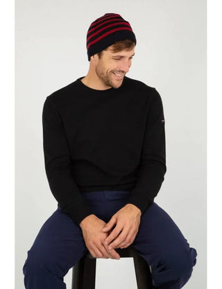 Man wearing a navy and red striped wool beanie and black sweater sitting on a stool