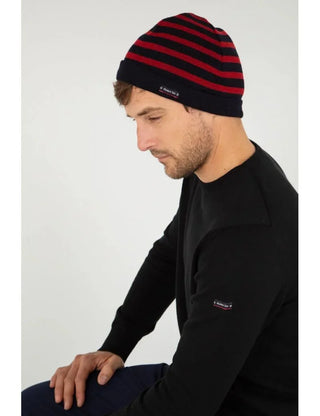 Man wearing a navy and red striped knit wool beanie and black sweater on light background