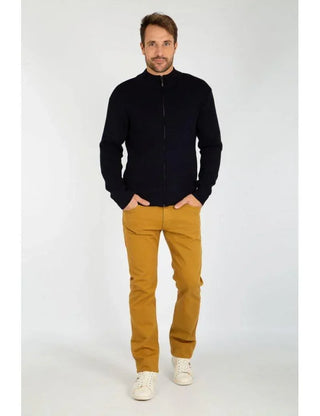 Man wearing a black zip-up wool cardigan, mustard pants, and white sneakers, standing indoors