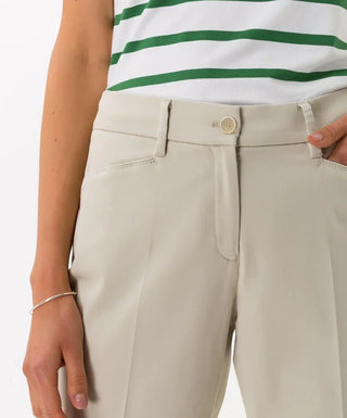 Close-up of beige cotton satin capri pants with pockets and button closure, worn with striped top.