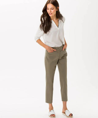 Woman wearing taupe cotton satin capri pants and a white blouse on a plain background