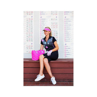 Woman in black golf shorts and top with pink visor and bag sitting in front of scoreboards