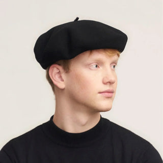 Man wearing a classic black Basque beret and black sweater, neutral background