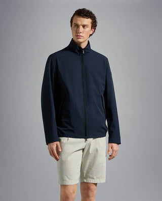 Man wearing a navy nylon zip-up jacket and beige shorts against a plain background