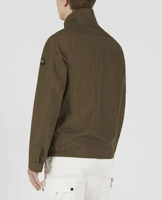 Man wearing olive green nylon jacket with patch on sleeve, white cargo pants, back view