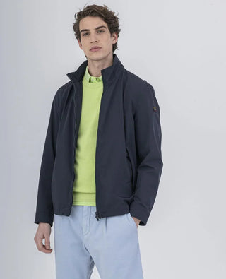 Man wearing navy nylon jacket over lime green sweater and light blue pants, studio background