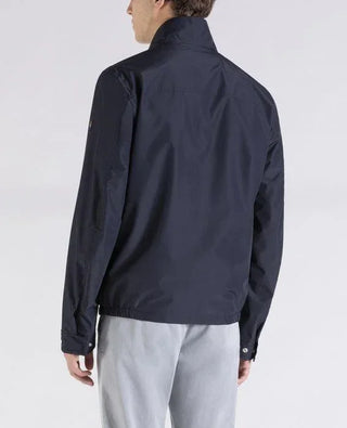 Man wearing navy nylon jacket and light gray pants, shown from the back, studio setting