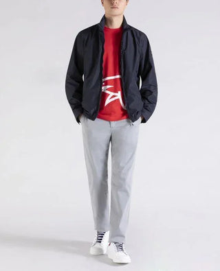 Man wearing navy nylon jacket, red graphic T-shirt, light gray pants, and white sneakers