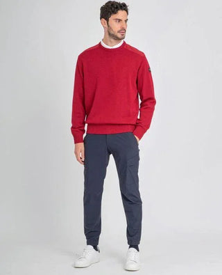 Man wearing a red crew neck sweater with shoulder patches, navy pants, and white sneakers