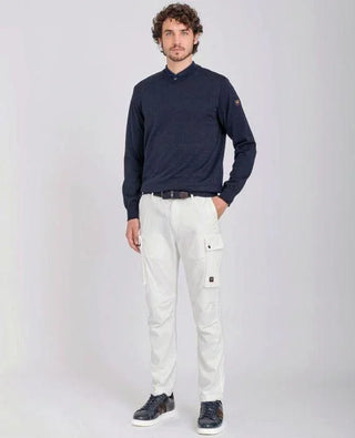 Man wearing navy merino wool V-neck sweater and white cargo pants, standing studio background