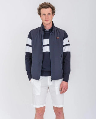 Man wearing a navy sleeveless vest, striped sweater, and white shorts on white background
