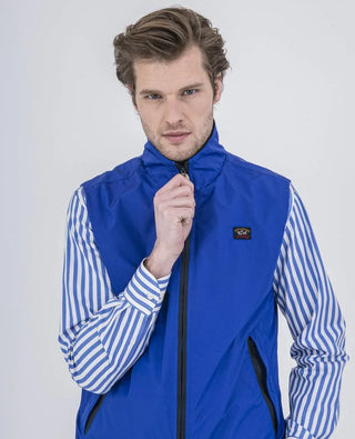 Man wearing a blue nylon sleeveless vest over a blue and white striped shirt
