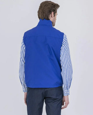 Man wearing blue nylon sleeveless vest, striped shirt, and dark pants, back view